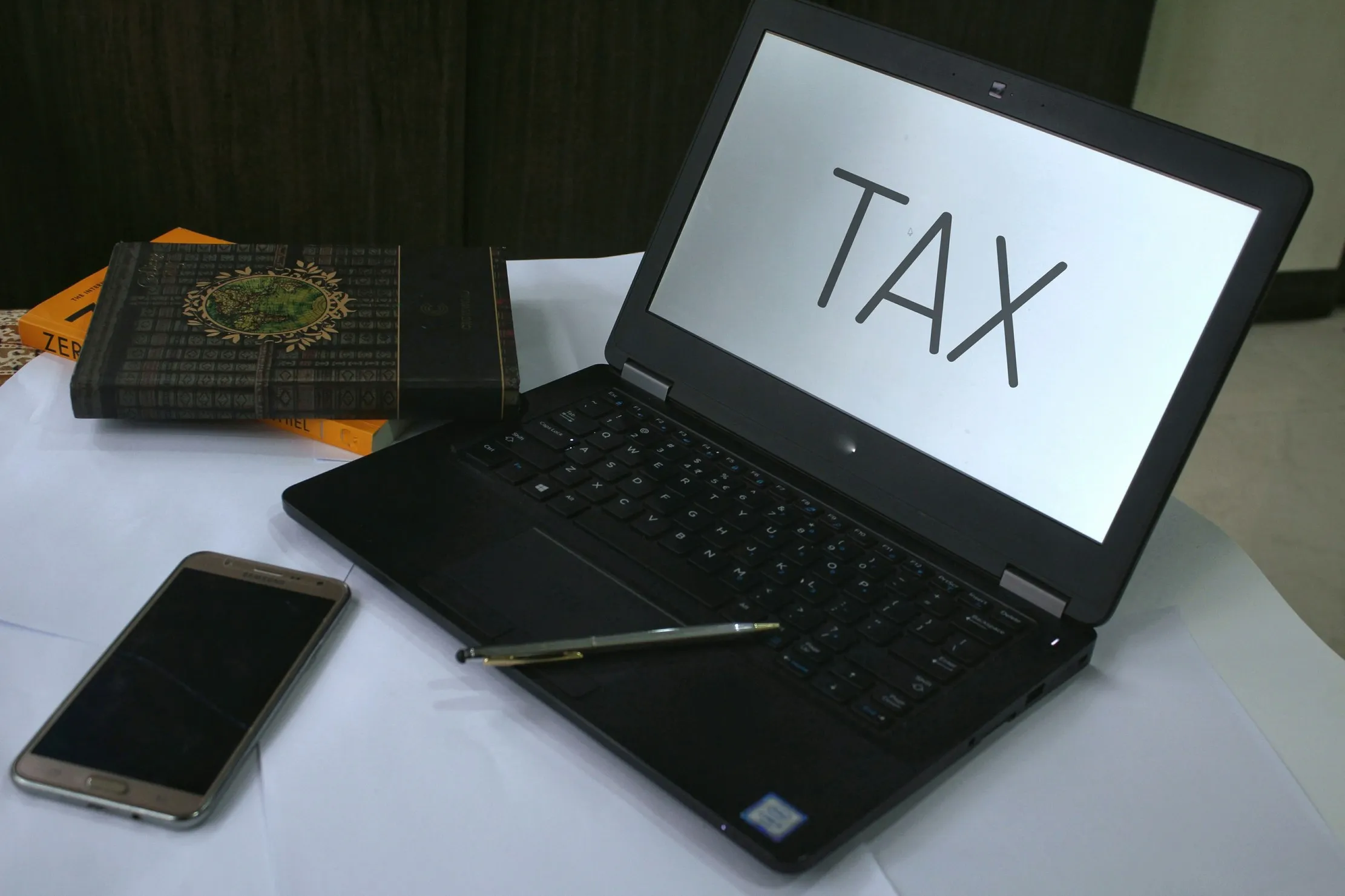 Laptop showing TAX beside a phone and books, representing the connection between electronic invoicing, source records and the ledger