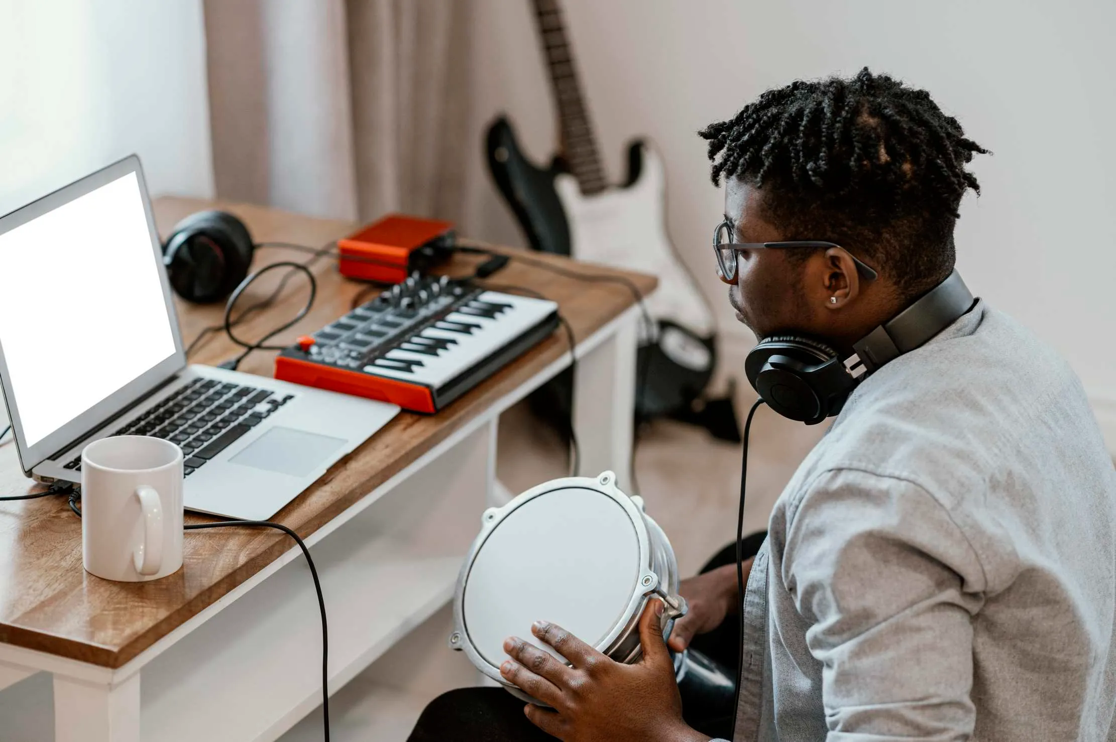 Musician at home playing drums and mixing with a laptop — home studio music production Uganda